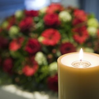 A lit memorial candle beside a wreath of flowers